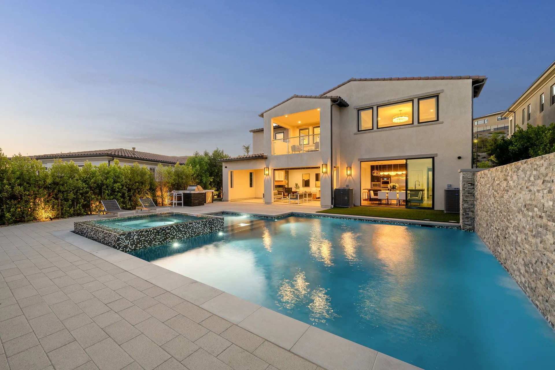 Luxury custom inground pool with spa and illuminated home at twilight, showcasing a finished residential backyard