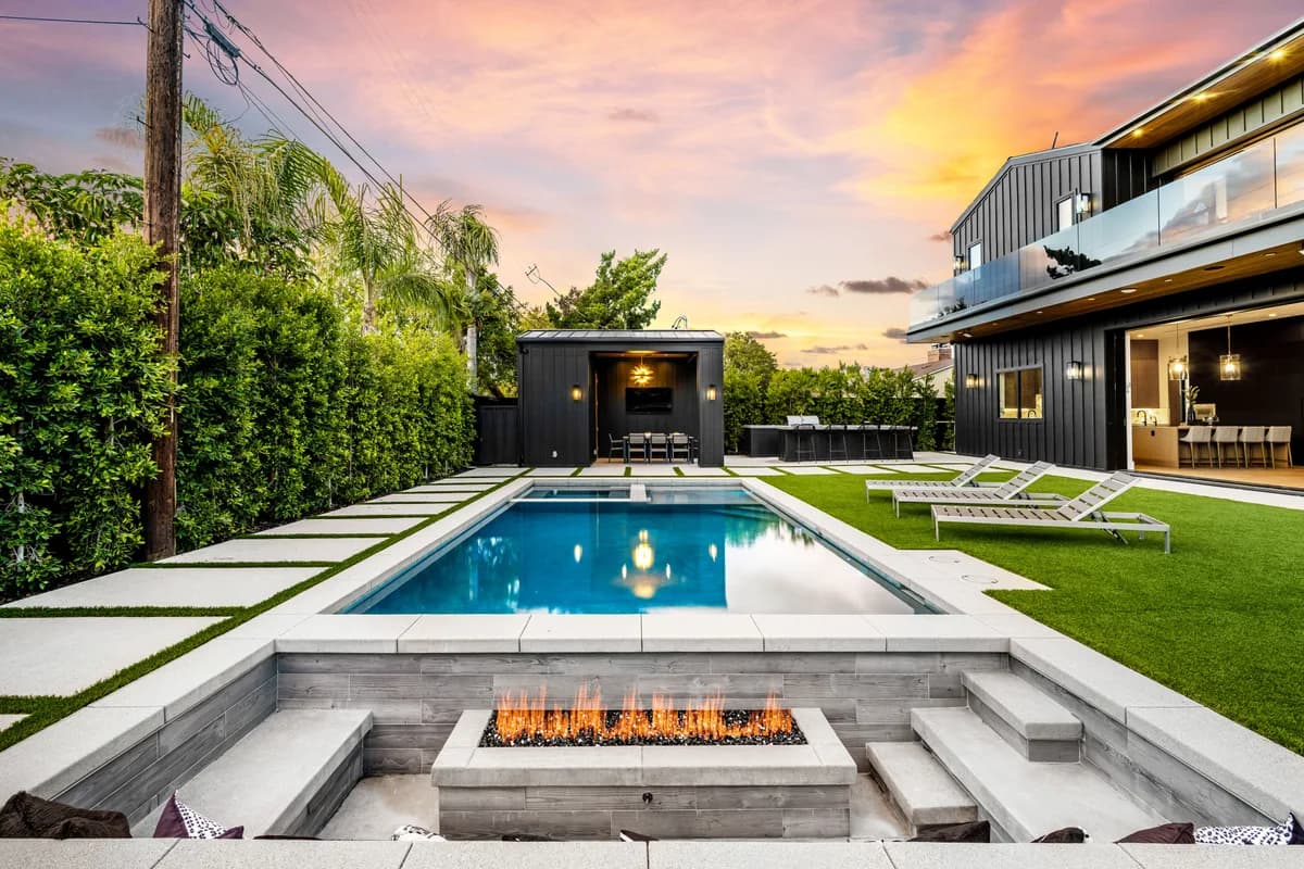 Custom backyard with a rectangular inground pool, fire pit feature, and lounge seating at sunset