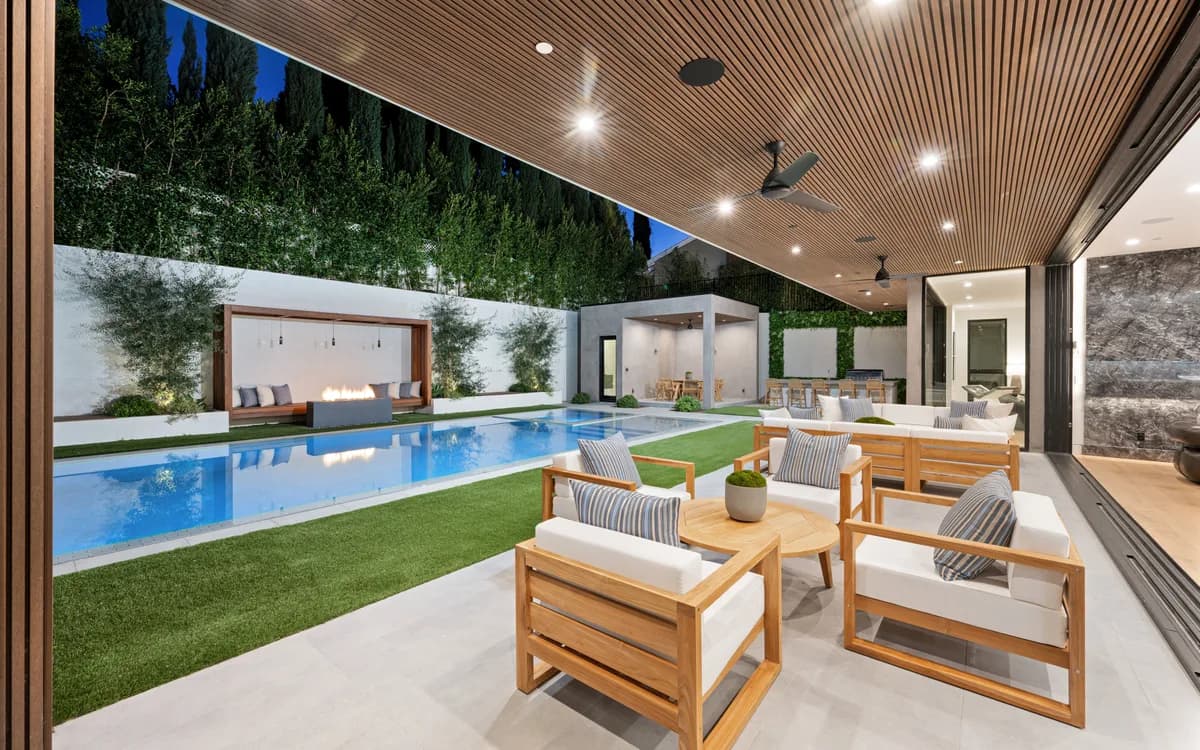Expansive modern outdoor living space with a long rectangular inground pool, covered patio, and lush landscaping